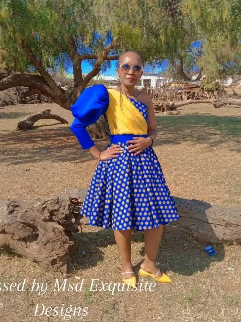 Woman in a custom cobalt blue one-shoulder puff-sleeve top with gold sash and polka-dot shweshwe circle skirt