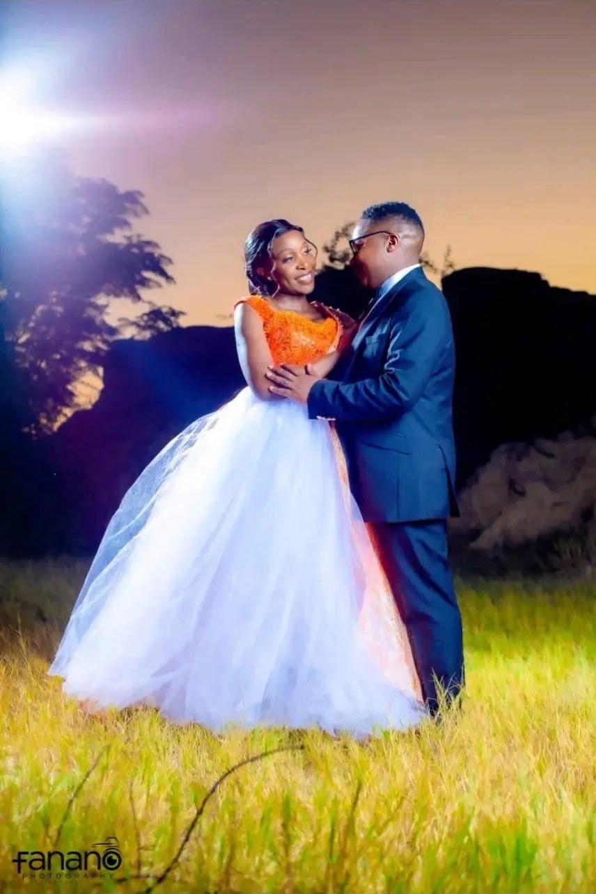 Bride wearing a custom white tulle ball gown with orange beaded lace bodice standing with her groom in a sunset field