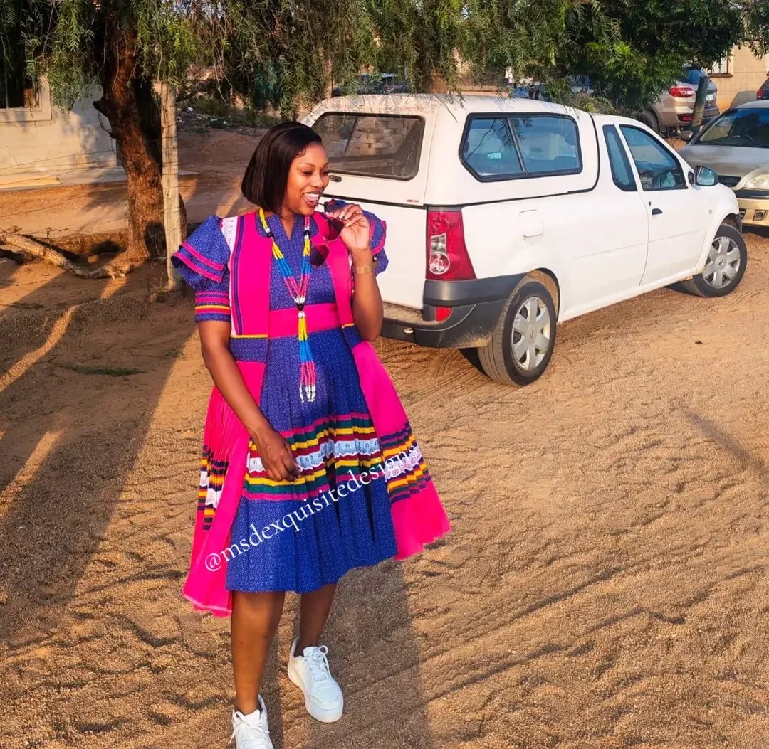 Woman wearing a custom Sepedi outfit in indigo shweshwe with pink pleated overlay, ribbon trim and beaded necklace